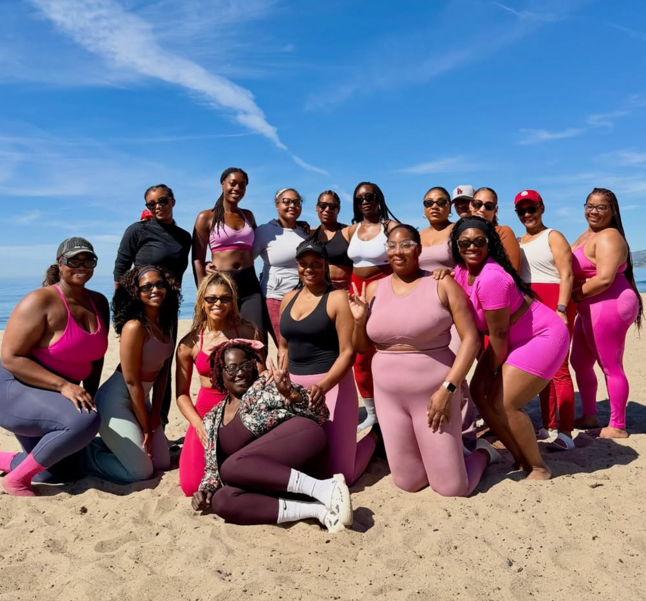 Group of women posing on a beach with a clear blue sky.