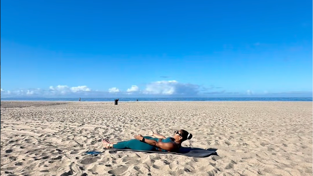 Person lying on a towel on a sandy beach with a clear blue sky